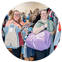 Three generations shop together at their local JBF sale. Mom carries baby in a baby carrier while grandmom stands behind them.